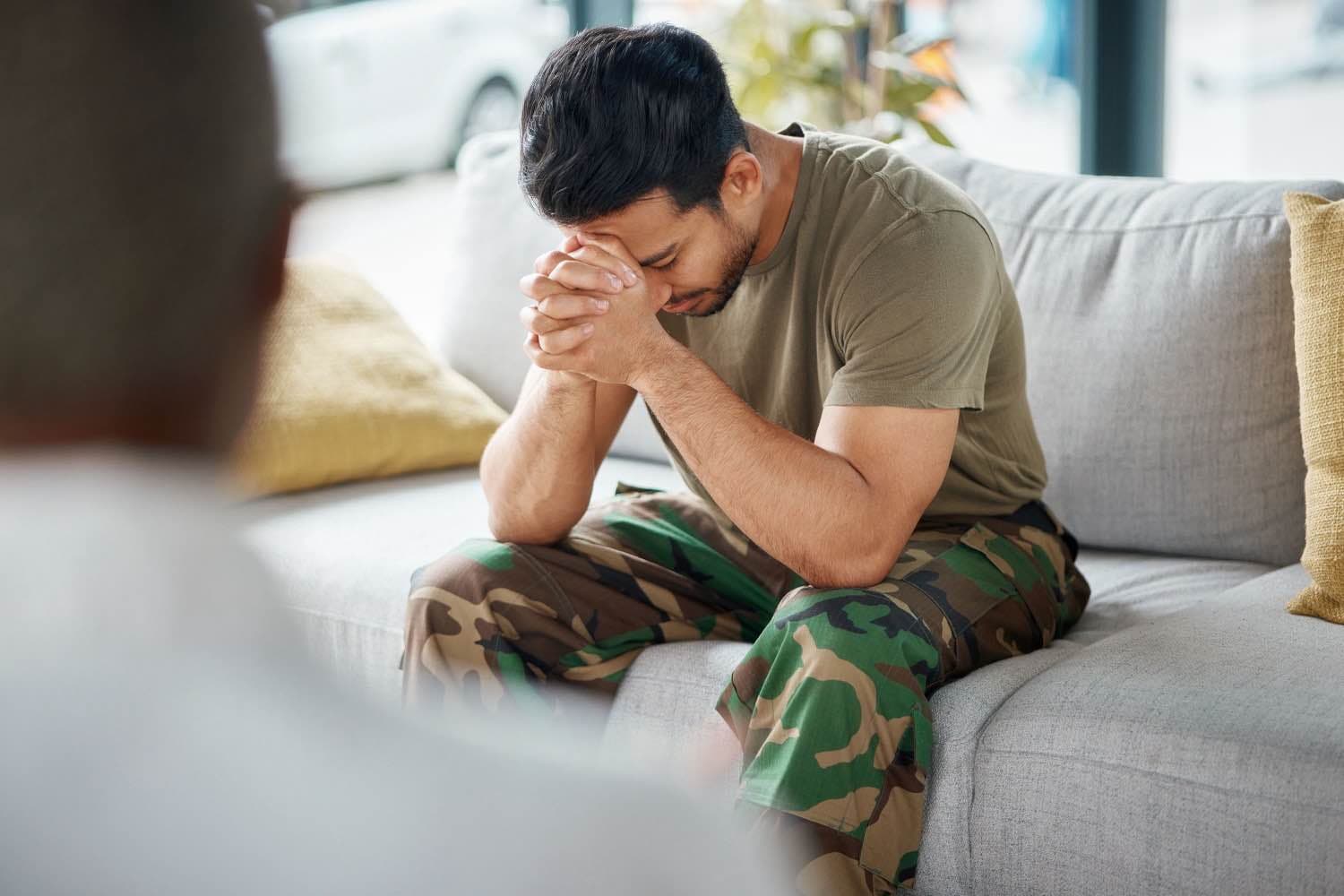 soldier sitting on the couch with his head resting on his hands.